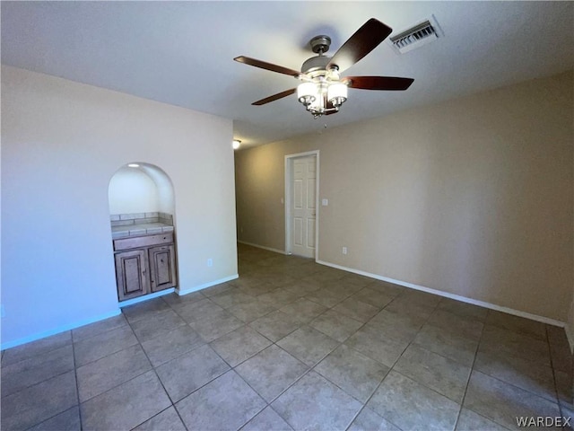 tiled empty room with ceiling fan, visible vents, and baseboards