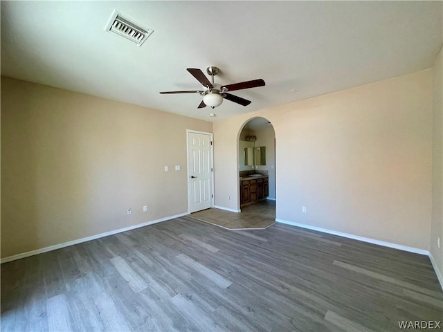 unfurnished room with baseboards, visible vents, a ceiling fan, arched walkways, and wood finished floors