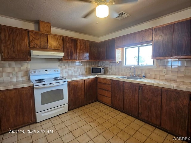 kitchen with stainless steel microwave, electric stove, tile counters, and ventilation hood