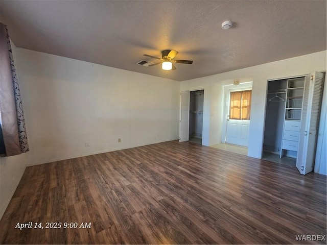unfurnished bedroom featuring visible vents, multiple closets, ceiling fan, and wood finished floors