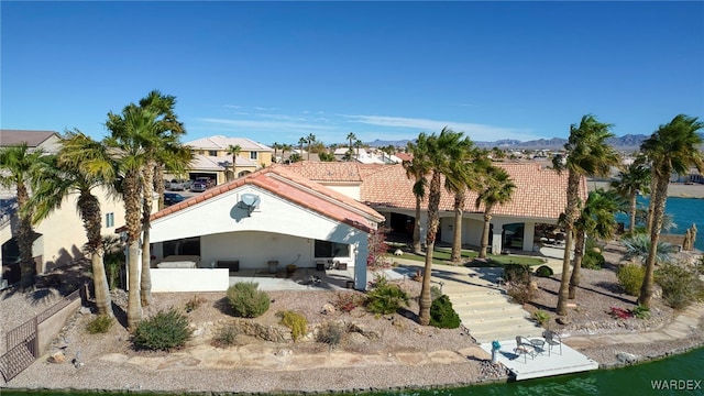 rear view of house featuring stucco siding, a water view, a patio area, fence, and a tiled roof