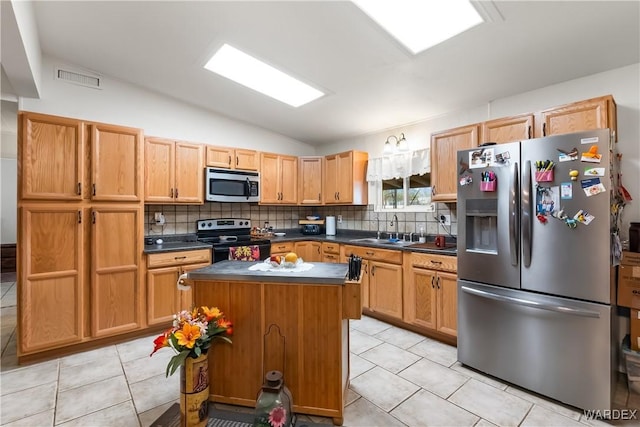 kitchen featuring lofted ceiling, stainless steel appliances, a sink, a kitchen island, and dark countertops