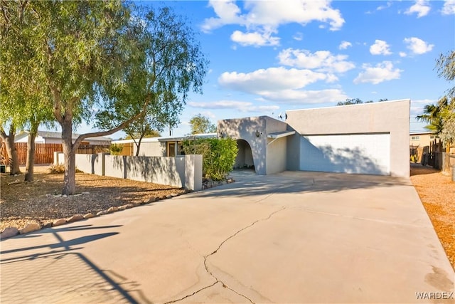 pueblo-style house with a garage, fence, driveway, and stucco siding