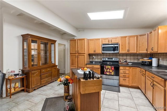 kitchen with a center island, stainless steel appliances, dark countertops, lofted ceiling, and backsplash