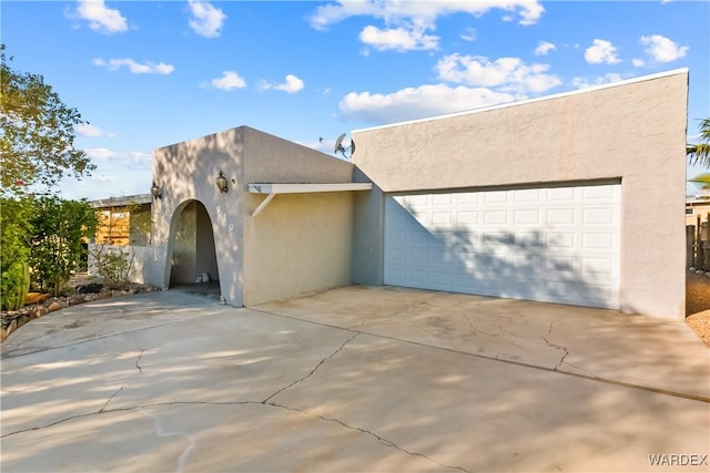 pueblo-style house with a garage, concrete driveway, and stucco siding