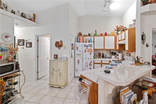 kitchen with white appliances, light tile patterned floors, tile counters, rail lighting, and under cabinet range hood