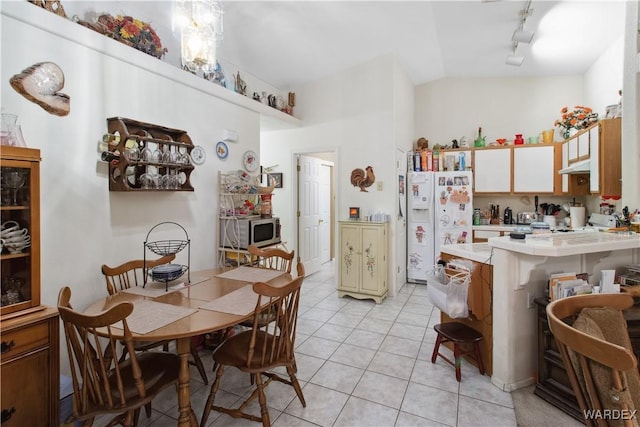 kitchen featuring light tile patterned floors, white refrigerator with ice dispenser, lofted ceiling, stainless steel microwave, and light countertops