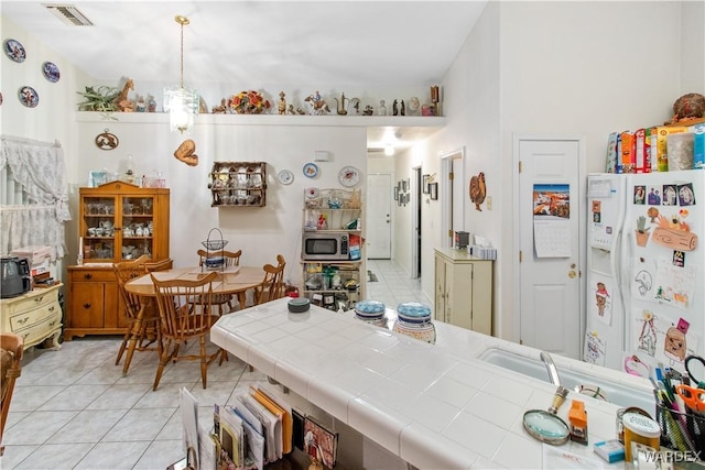 kitchen with light tile patterned floors, visible vents, tile counters, stainless steel microwave, and white fridge with ice dispenser