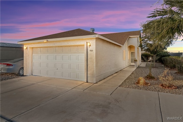 view of front facade featuring an attached garage, driveway, a shingled roof, and stucco siding