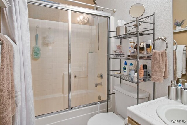 full bath with vanity, toilet, and bath / shower combo with glass door