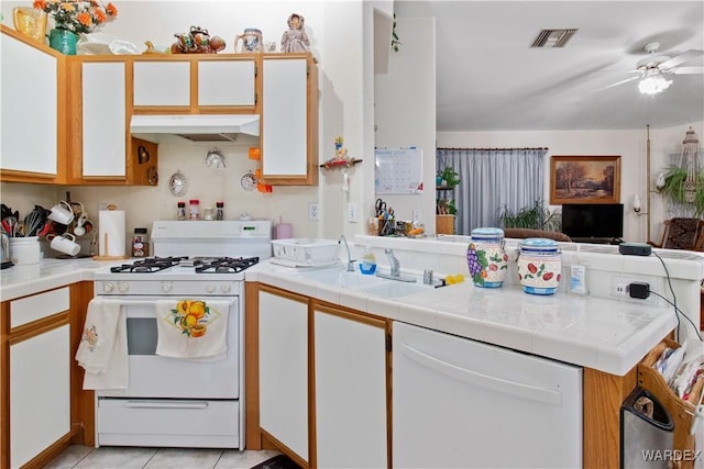 kitchen with white appliances, under cabinet range hood, tile counters, and white cabinets