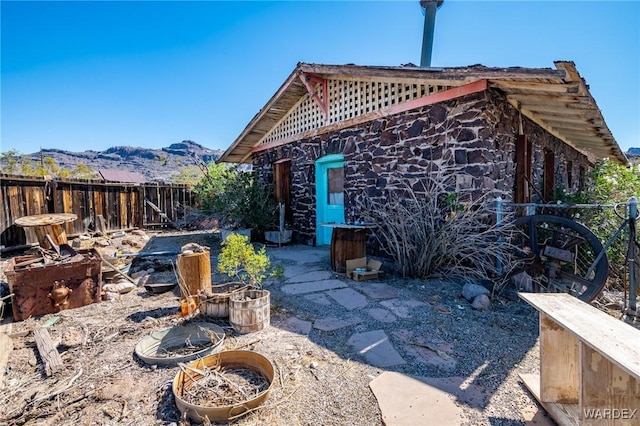 rear view of house with a mountain view, fence, a fire pit, and stone siding