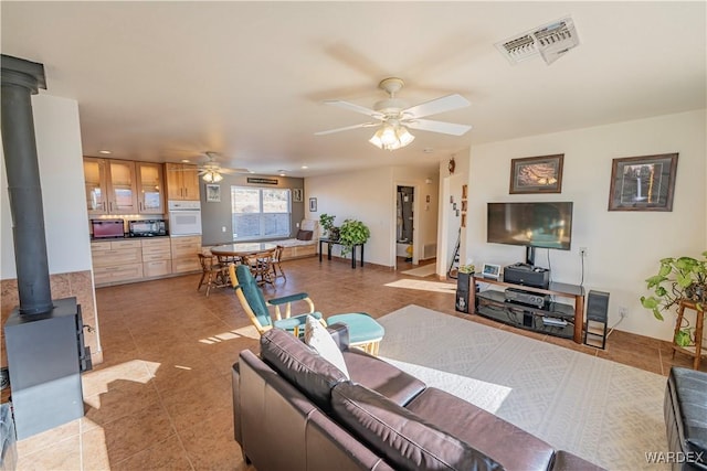 living room with a wood stove, visible vents, ceiling fan, and light tile patterned flooring