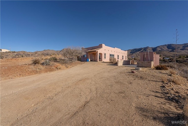 view of front of house with dirt driveway, a mountain view, and stucco siding