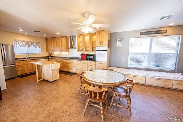 kitchen featuring visible vents, wall chimney exhaust hood, a center island, black appliances, and a sink