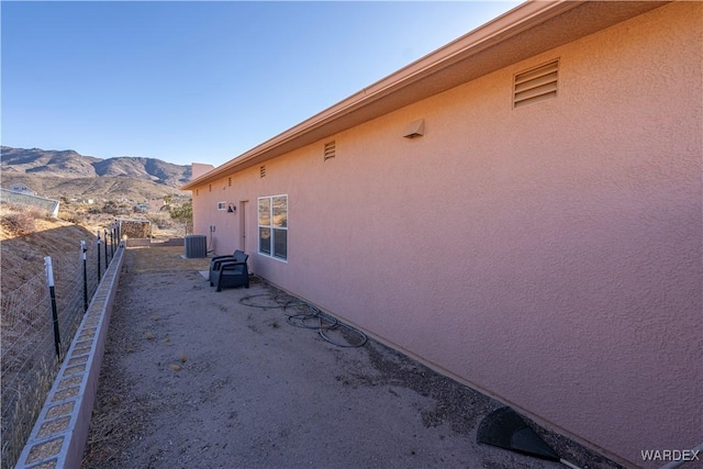 view of property exterior featuring central AC unit, fence, a mountain view, and stucco siding