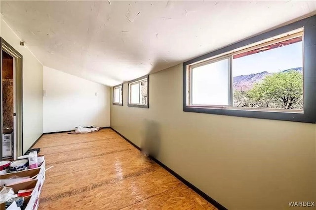 additional living space featuring lofted ceiling, light wood finished floors, a mountain view, and baseboards