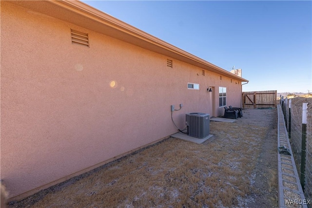 view of side of property featuring central AC unit, a fenced backyard, and stucco siding