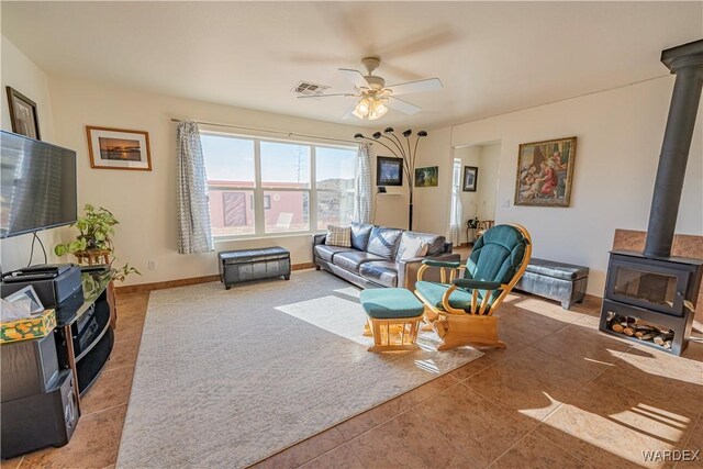 living room featuring visible vents, baseboards, a ceiling fan, tile patterned floors, and a wood stove