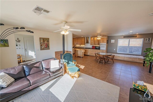 living room featuring ceiling fan, tile patterned flooring, visible vents, and a wood stove