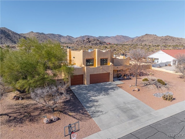 pueblo revival-style home featuring an attached garage, a mountain view, concrete driveway, and stucco siding