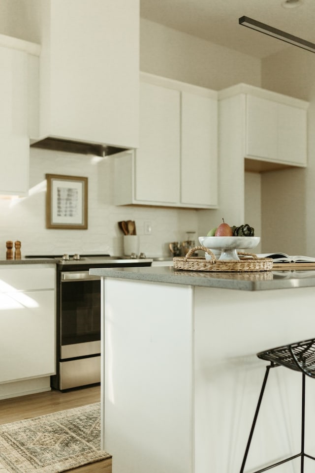 kitchen featuring white cabinetry, light hardwood / wood-style flooring, stainless steel stove, and tasteful backsplash