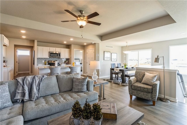 living room with light wood finished floors, baseboards, visible vents, and recessed lighting