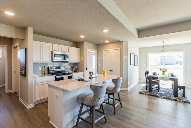 kitchen with stainless steel appliances, light countertops, white cabinets, and a kitchen island with sink