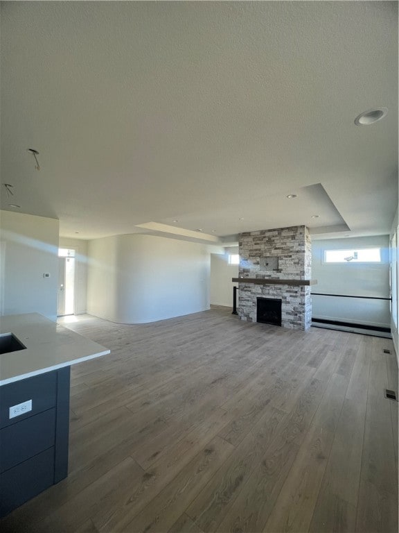 unfurnished living room with hardwood / wood-style floors, a textured ceiling, and a stone fireplace