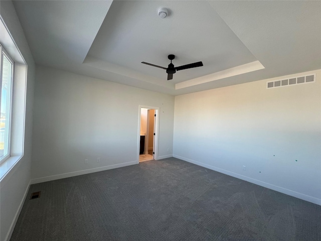 carpeted spare room featuring a tray ceiling and ceiling fan