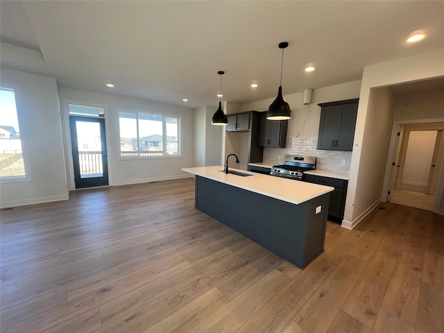 kitchen with an island with sink, sink, decorative backsplash, light hardwood / wood-style floors, and stainless steel range oven