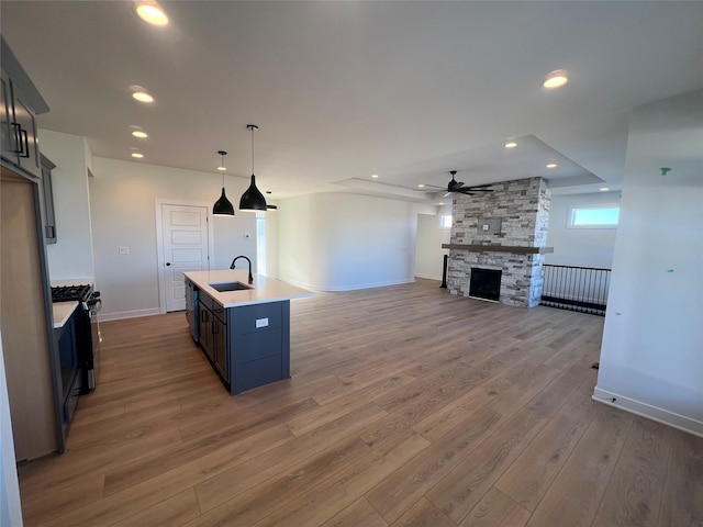 kitchen featuring a stone fireplace, hardwood / wood-style floors, pendant lighting, an island with sink, and sink