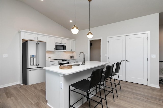 kitchen featuring white cabinets, hanging light fixtures, sink, appliances with stainless steel finishes, and a breakfast bar area