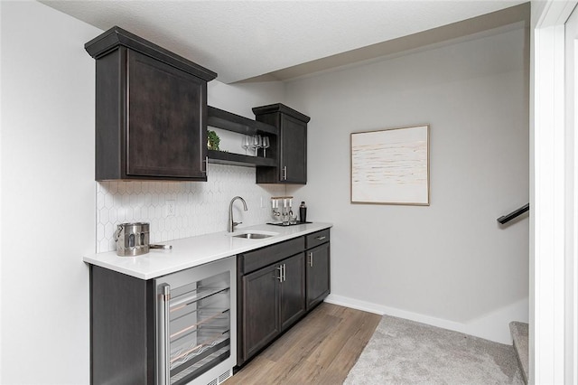 kitchen with sink, wine cooler, light hardwood / wood-style flooring, tasteful backsplash, and dark brown cabinetry