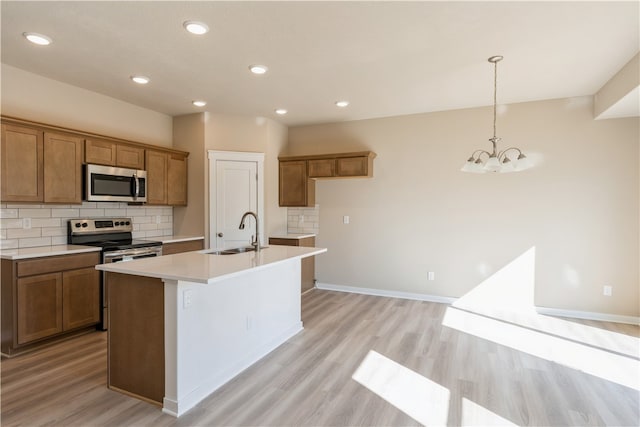 kitchen featuring an island with sink, tasteful backsplash, stainless steel appliances, an inviting chandelier, and light wood-type flooring