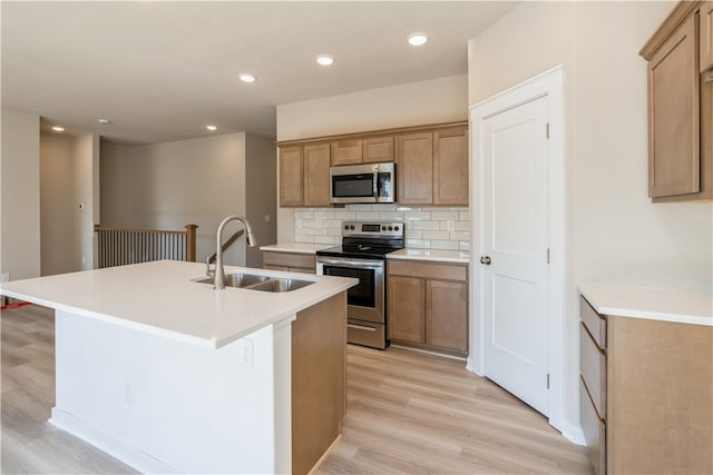 kitchen featuring a kitchen island with sink, sink, light hardwood / wood-style flooring, backsplash, and stainless steel appliances