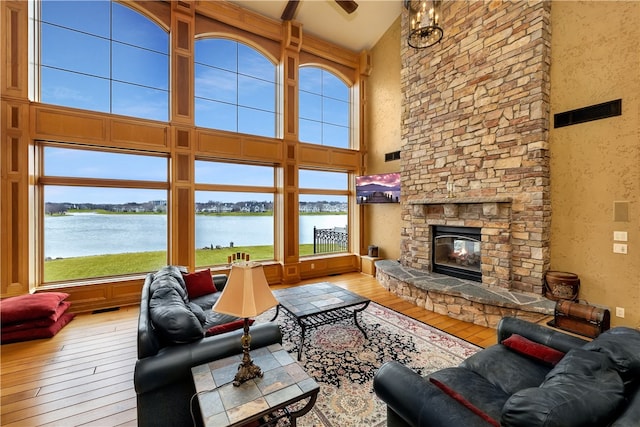 living room with a high ceiling, ceiling fan, a fireplace, a water view, and light wood-type flooring