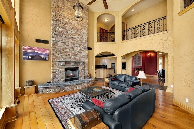 living room with a high ceiling, a stone fireplace, wood-type flooring, and ceiling fan