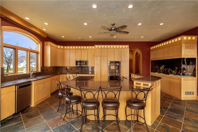 kitchen with stainless steel appliances, a kitchen island, ceiling fan, a breakfast bar area, and sink