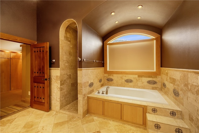 bathroom featuring tiled bath, tile walls, tile flooring, and lofted ceiling