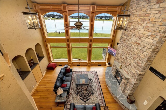 unfurnished living room with a stone fireplace, ceiling fan with notable chandelier, a wealth of natural light, and light wood-type flooring