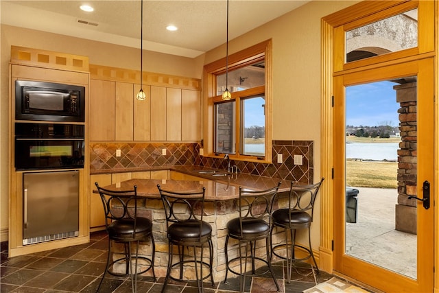 kitchen featuring a breakfast bar area, a water view, tasteful backsplash, and black appliances