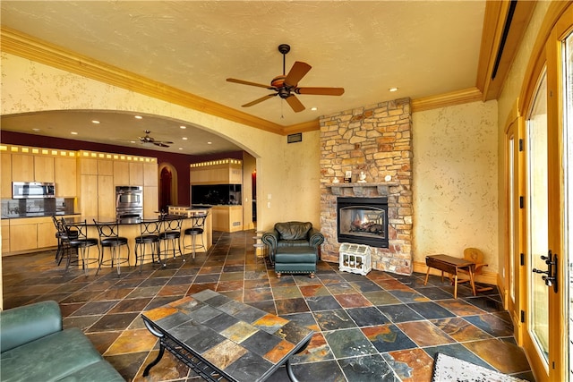 tiled living room with a stone fireplace, ceiling fan, and ornamental molding