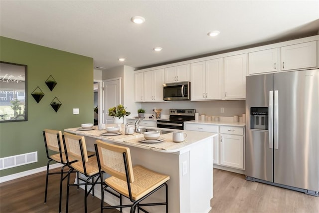 kitchen with a kitchen bar, white cabinetry, light hardwood / wood-style flooring, appliances with stainless steel finishes, and an island with sink