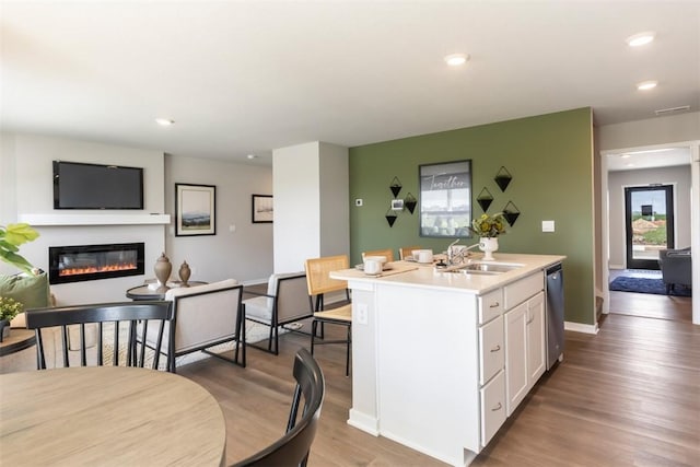 kitchen featuring wood-type flooring, sink, white cabinets, stainless steel dishwasher, and a center island with sink