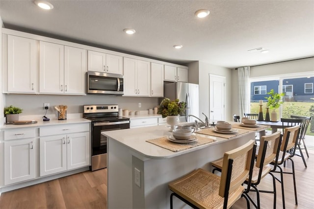 kitchen with a center island with sink, light hardwood / wood-style floors, white cabinets, and appliances with stainless steel finishes