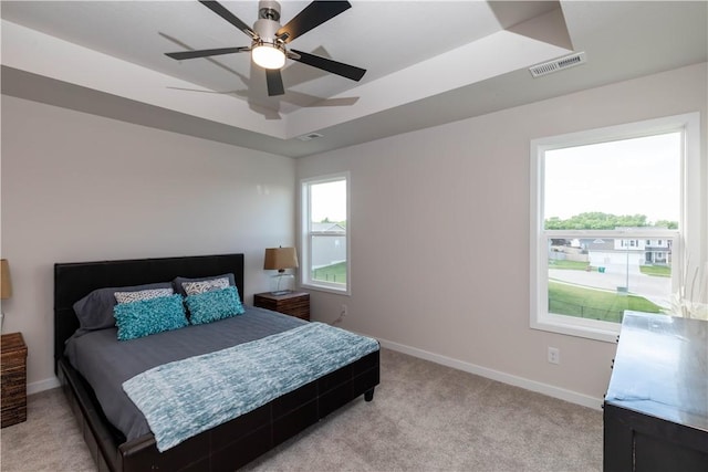 bedroom featuring a raised ceiling, ceiling fan, and light carpet