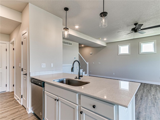 kitchen featuring light stone countertops, white cabinetry, hanging light fixtures, dishwasher, and sink