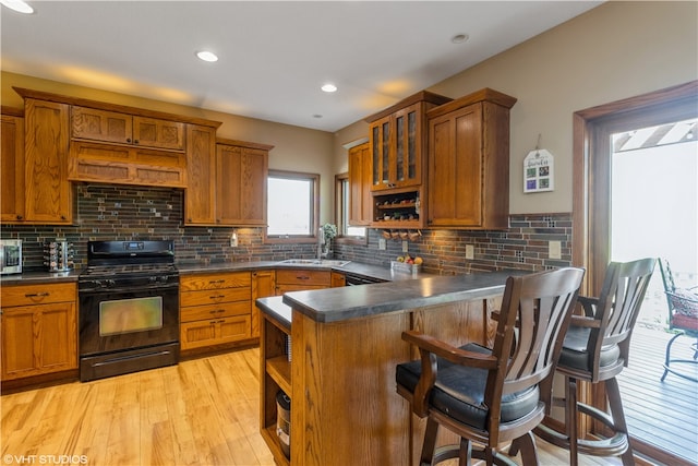 kitchen featuring black range with gas stovetop, tasteful backsplash, a breakfast bar, and light hardwood / wood-style flooring