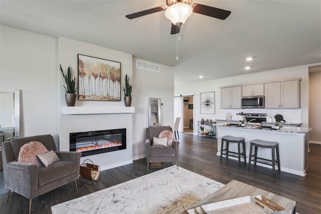 living room with a barn door, dark wood-type flooring, and ceiling fan